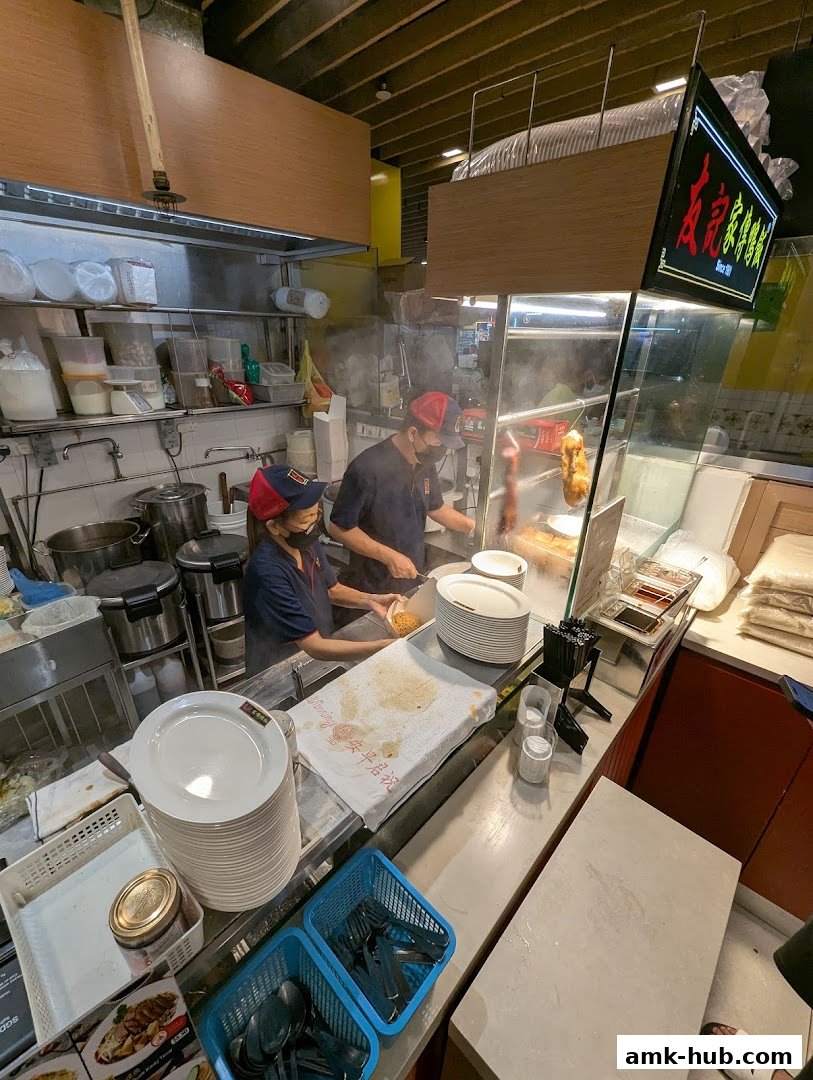 Two chefs preparing food behind a counter with stacks of plates and kitchen equipment.