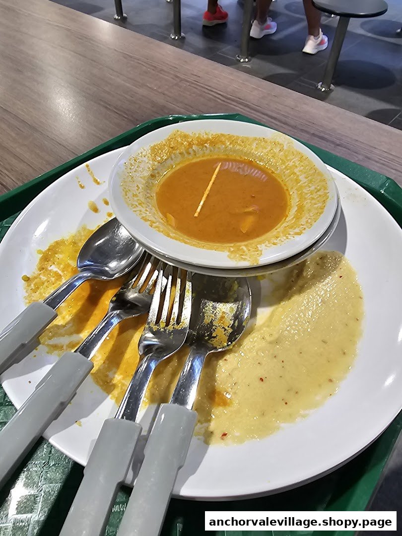 A used plate with leftover Indian curry and cutlery on a table, suggesting a recently finished meal.