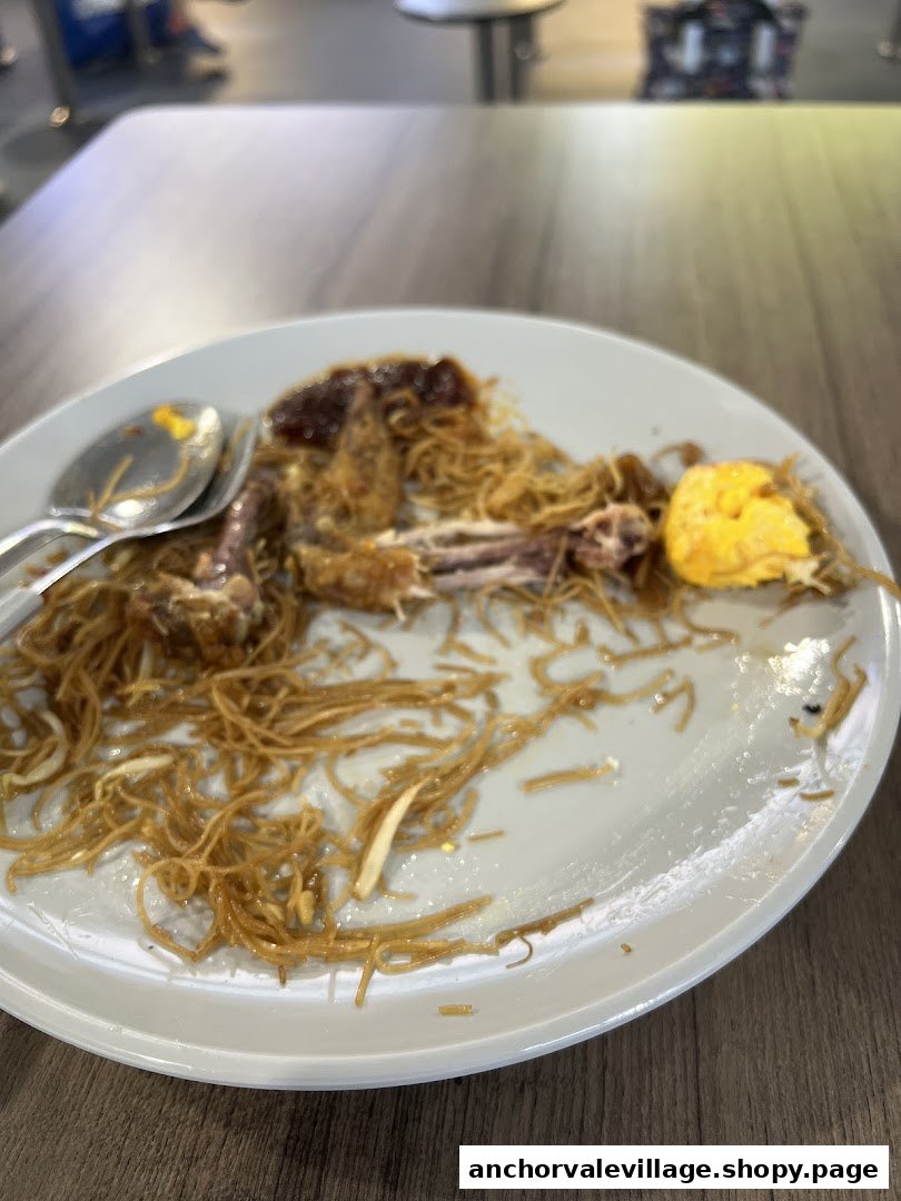 A plate with remnants of a finished meal, including noodles, bones, and egg, on a wooden table.