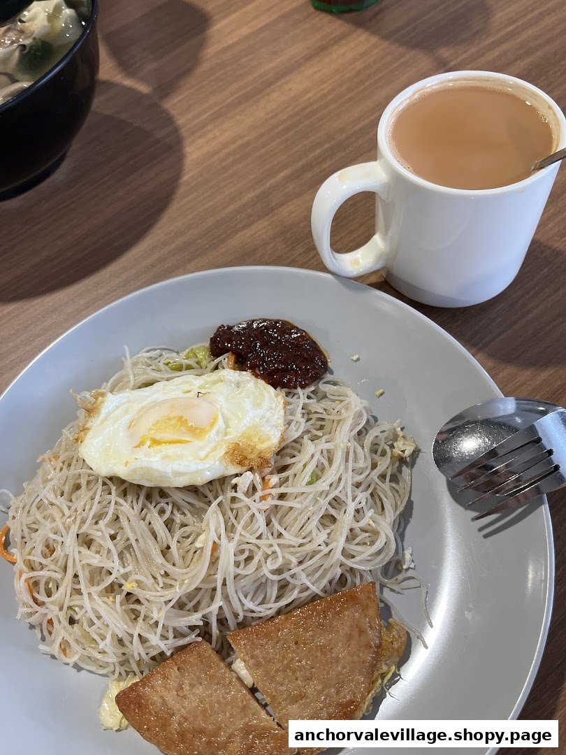 A plate of fried vermicelli with a fried egg, luncheon meat, chili, and a cup of milk tea.