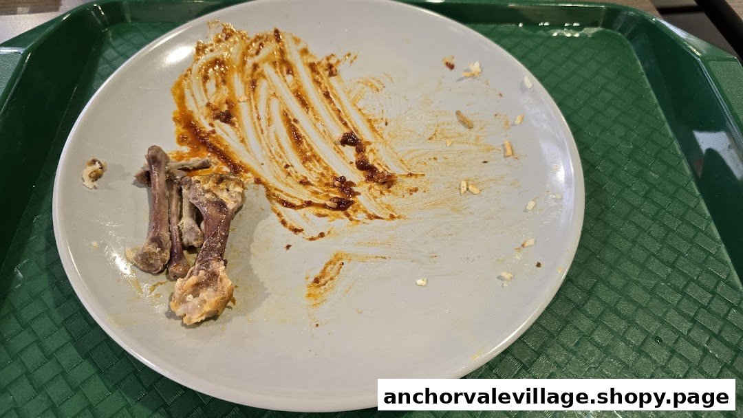 A grey plate with chicken bones and chili sauce remnants on a green tray, indicating a finished meal.