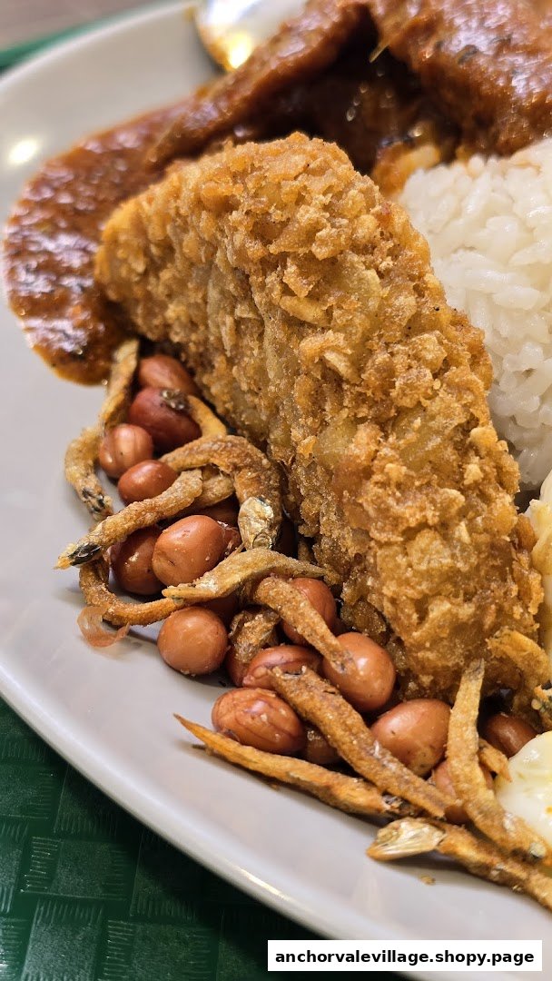 A close-up of Nasi Lemak featuring crispy fried fish, anchovies, peanuts, and sambal.
