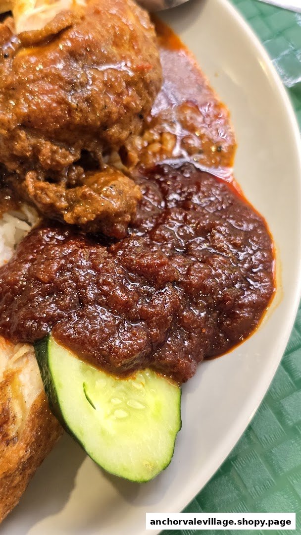 A close-up of delicious Nasi Lemak with chicken rendang, rich sambal, and fresh cucumber.