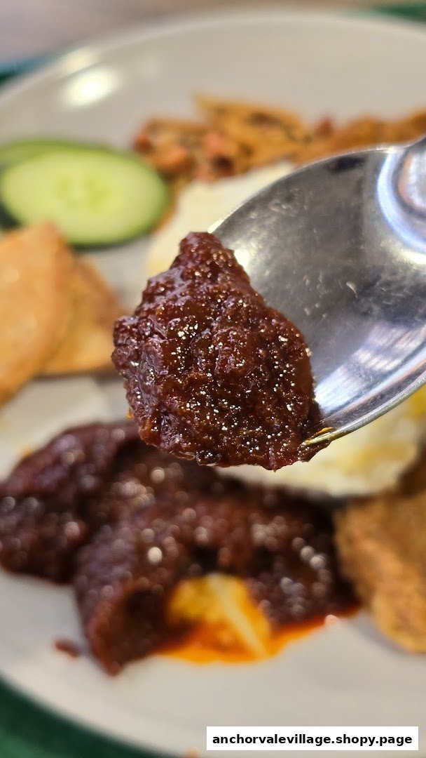 Close-up of rich, spicy sambal on a spoon, part of a Nasi Lemak dish.