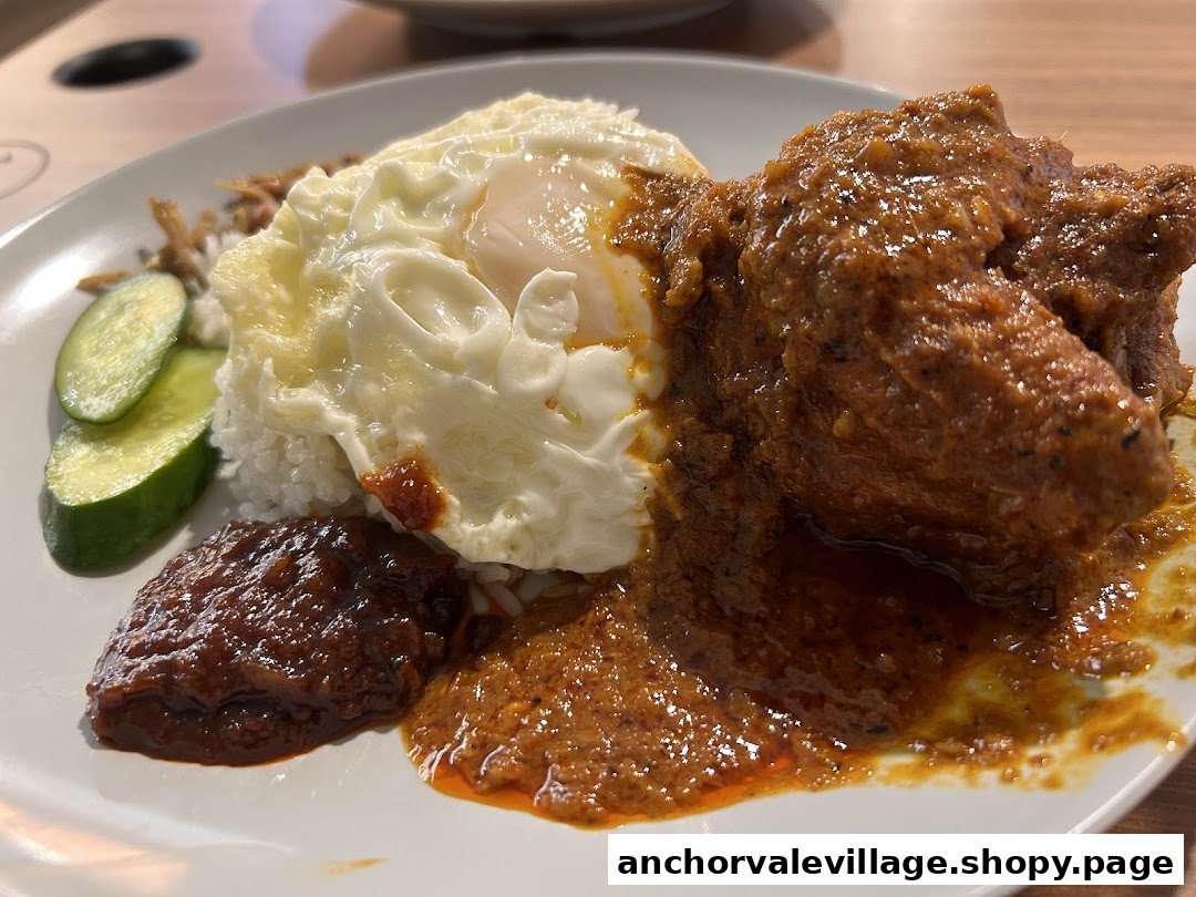 A close-up of a delicious Nasi Lemak plate featuring chicken rendang, fried egg, sambal, and cucumber.
