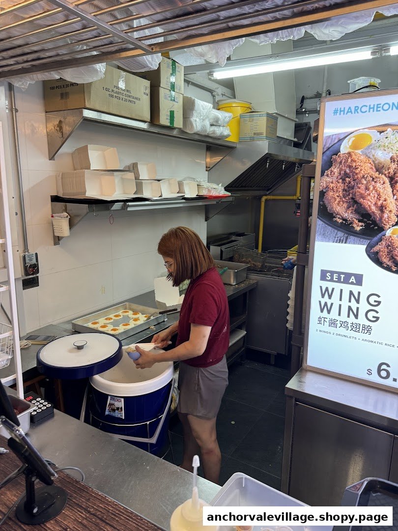 A staff member prepares food in the kitchen of AH TAN WINGS, with a menu display visible.