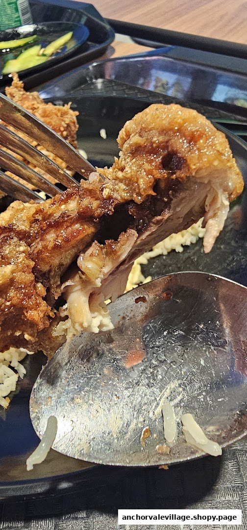 A close-up of a piece of crispy fried chicken being eaten with rice.