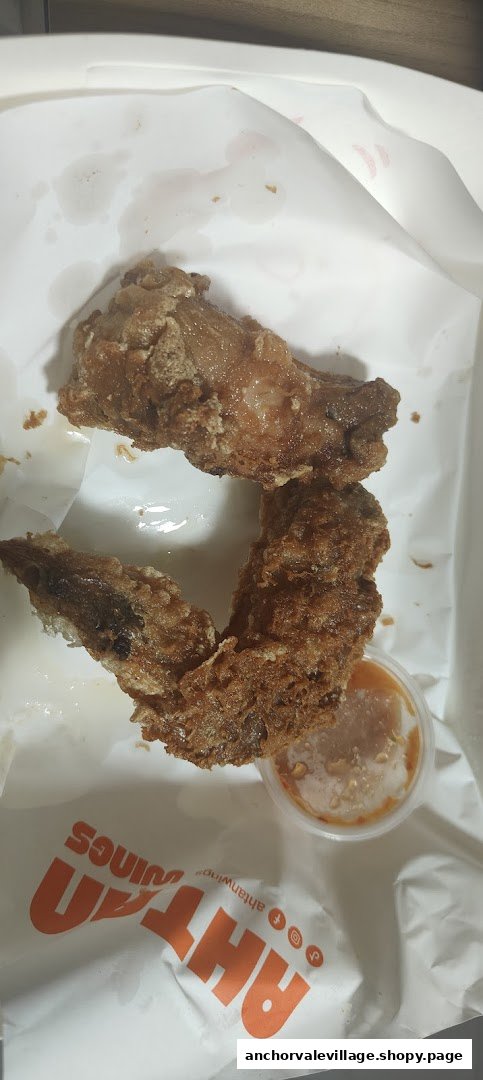 Two crispy fried chicken wings with a dipping sauce in a branded takeaway box from Ah Tan Wings.