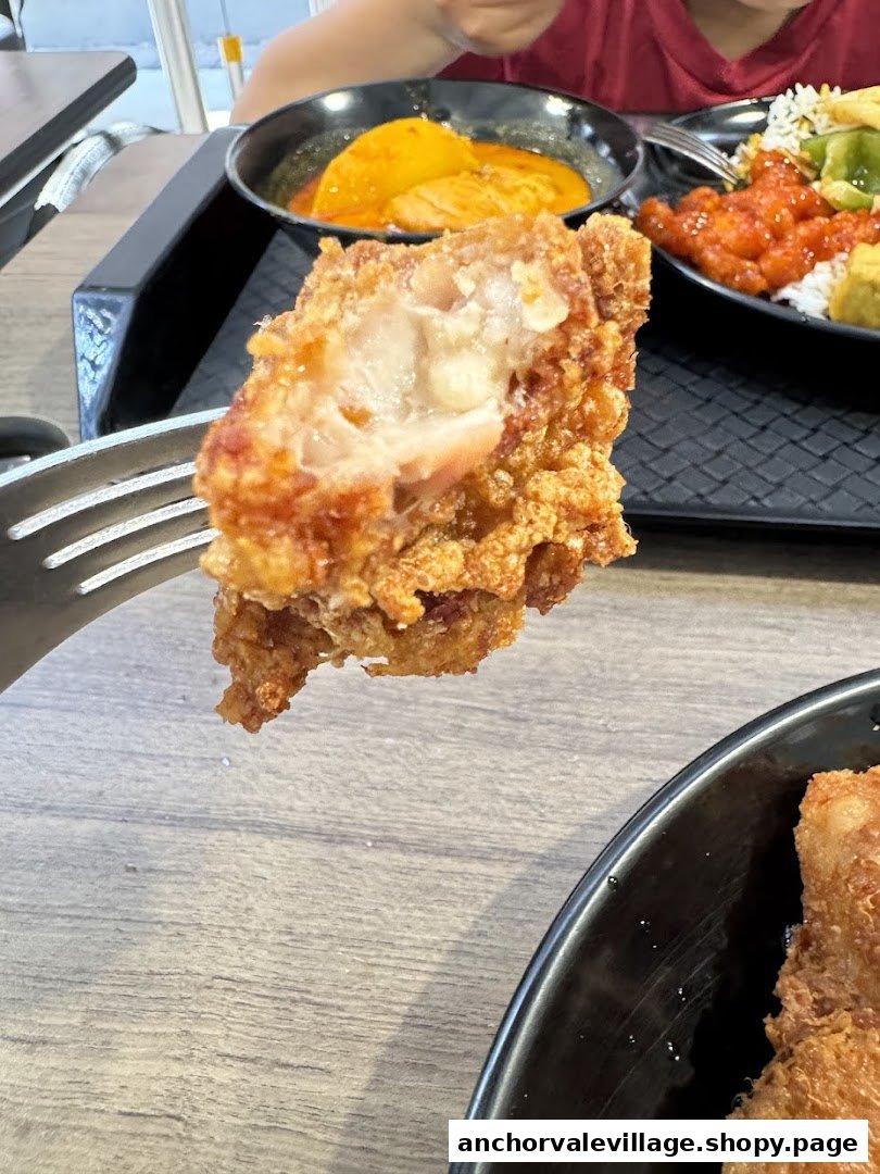 Close-up of a crispy fried chicken piece on a fork, with other delicious dishes in the background.