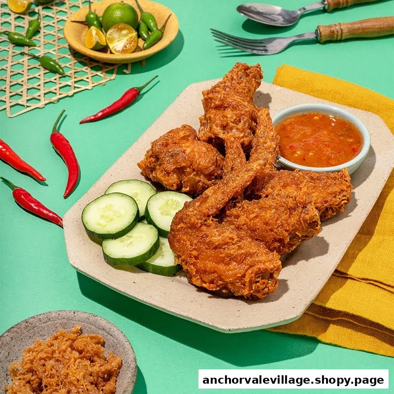 A plate of crispy fried chicken wings with cucumber slices and chili sauce, surrounded by fresh ingredients.