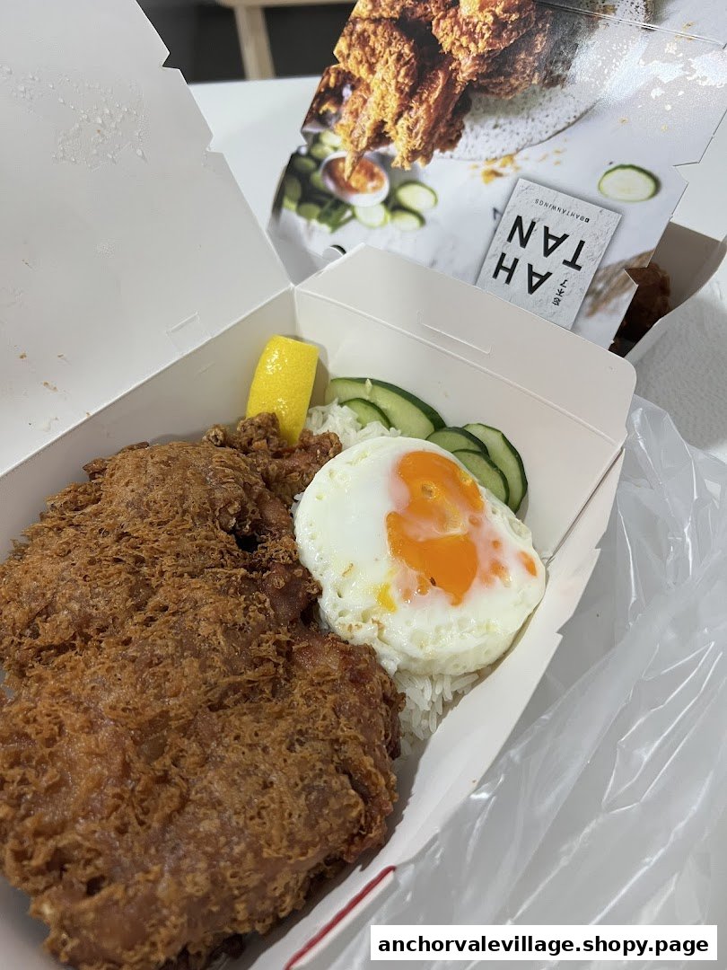 A crispy fried chicken cutlet with rice, sunny-side up egg, and cucumber in a takeaway box.