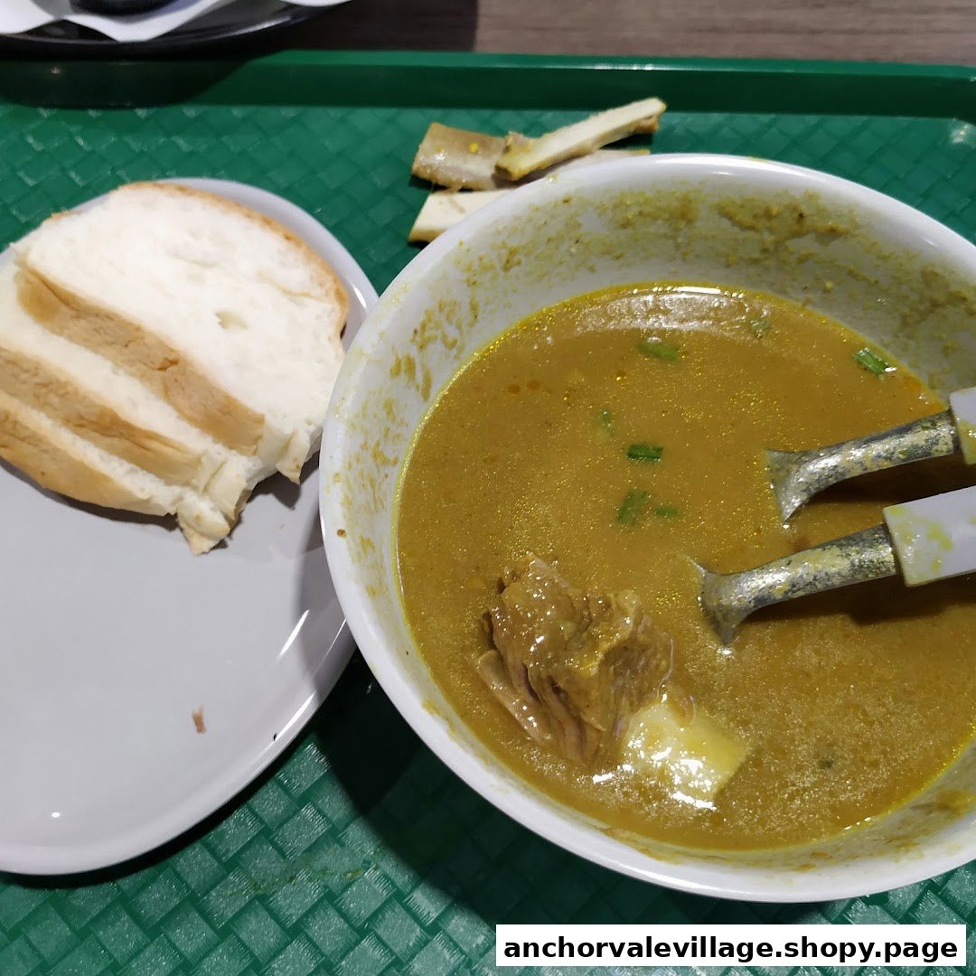 A bowl of mutton soup with bread slices and bones on a green tray.