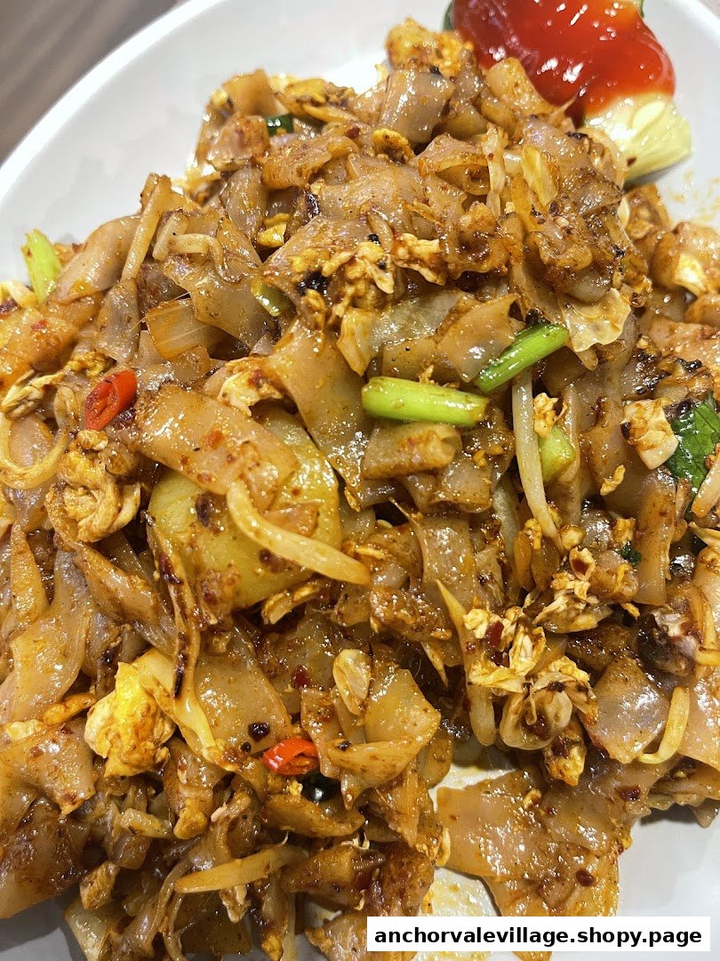 A close-up of delicious stir-fried flat noodles with egg, vegetables, and chili flakes.