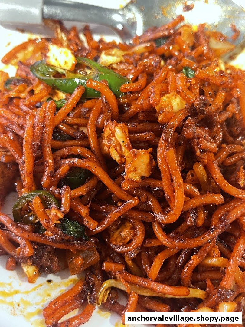 A close-up of spicy stir-fried noodles with green chilies and other ingredients.