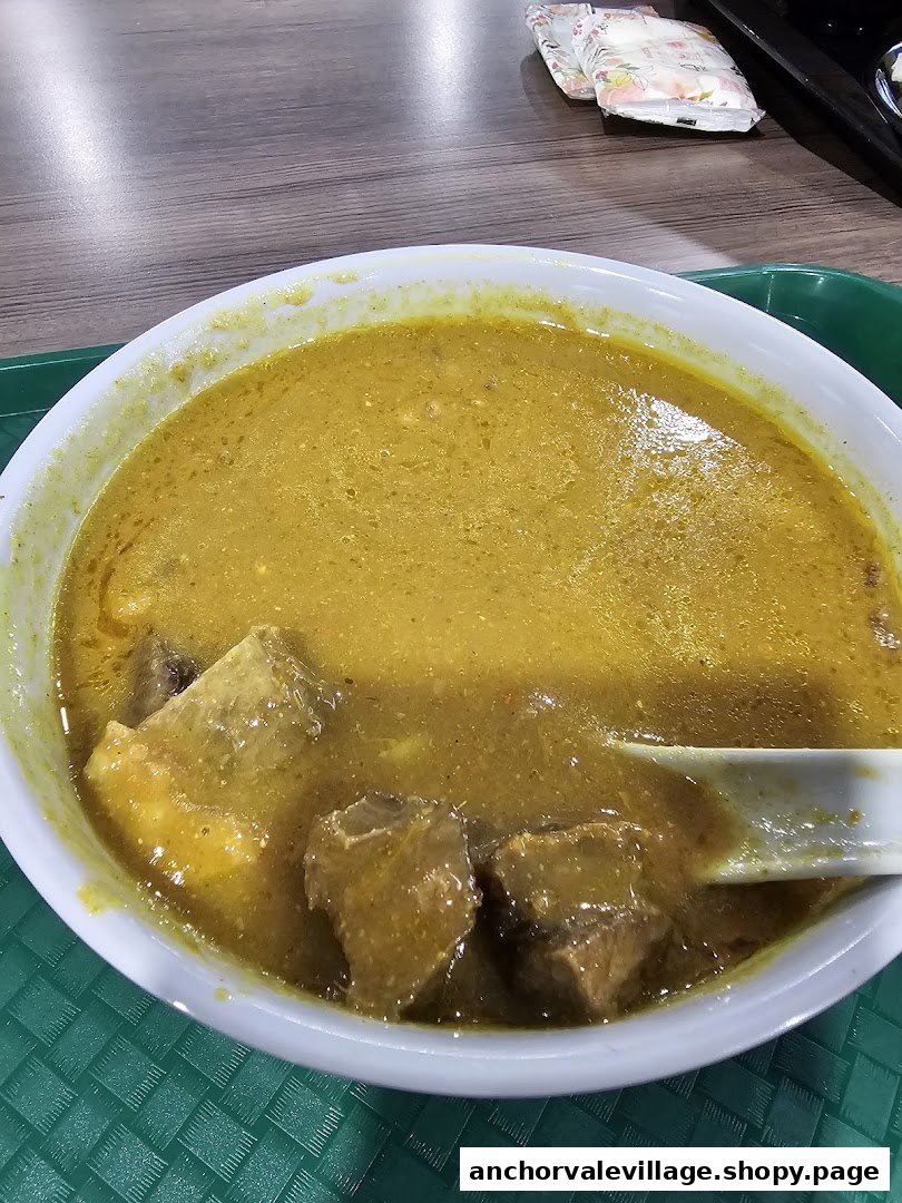 A close-up of a rich, yellow mutton soup with tender meat chunks in a white bowl.
