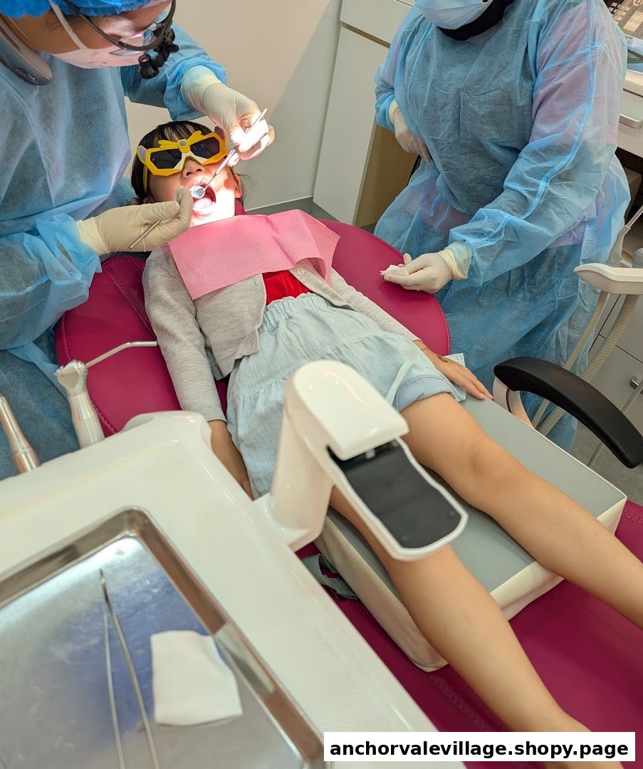 A child wearing protective glasses receives dental examination from a dentist and assistant.