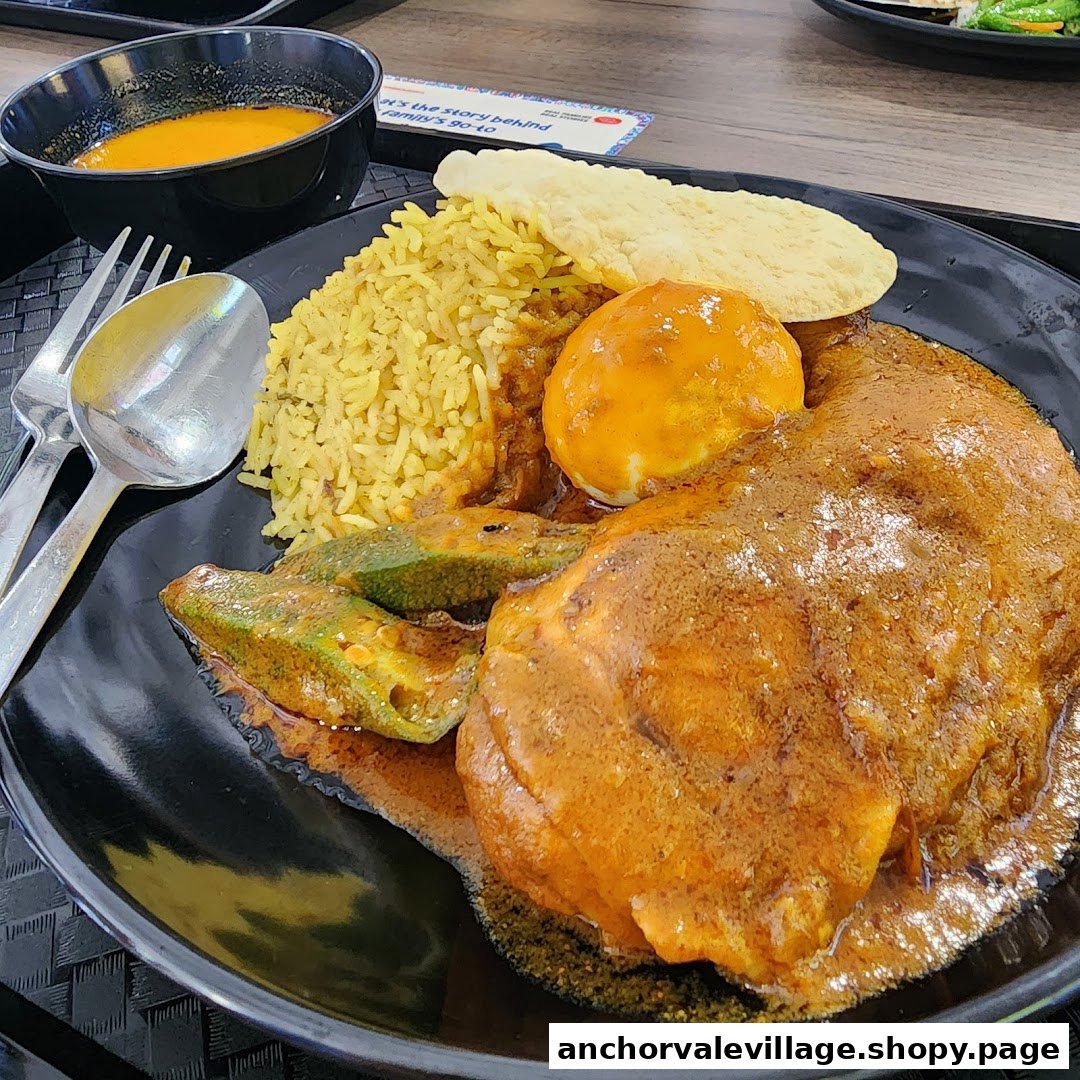 A vibrant plate of curry chicken with yellow rice, okra, and a hard-boiled egg, served with a side of soup.