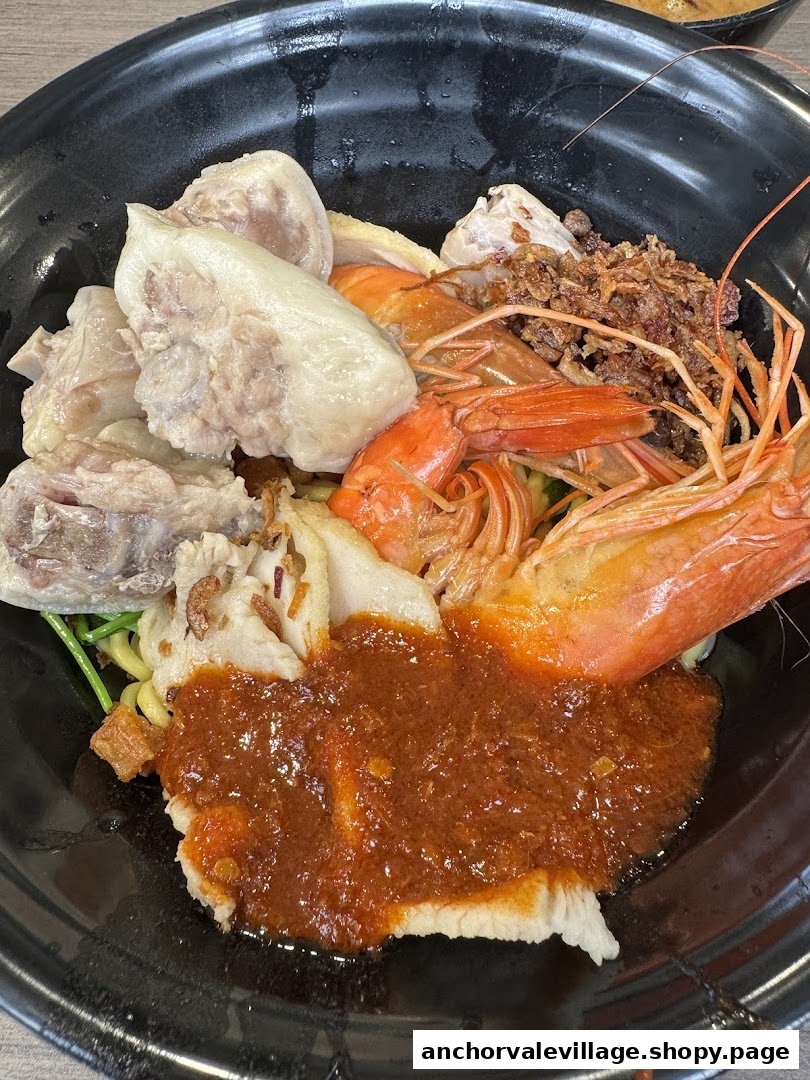 A vibrant bowl of hawker noodles featuring prawns, chicken, fishcake, and a rich chili sauce.
