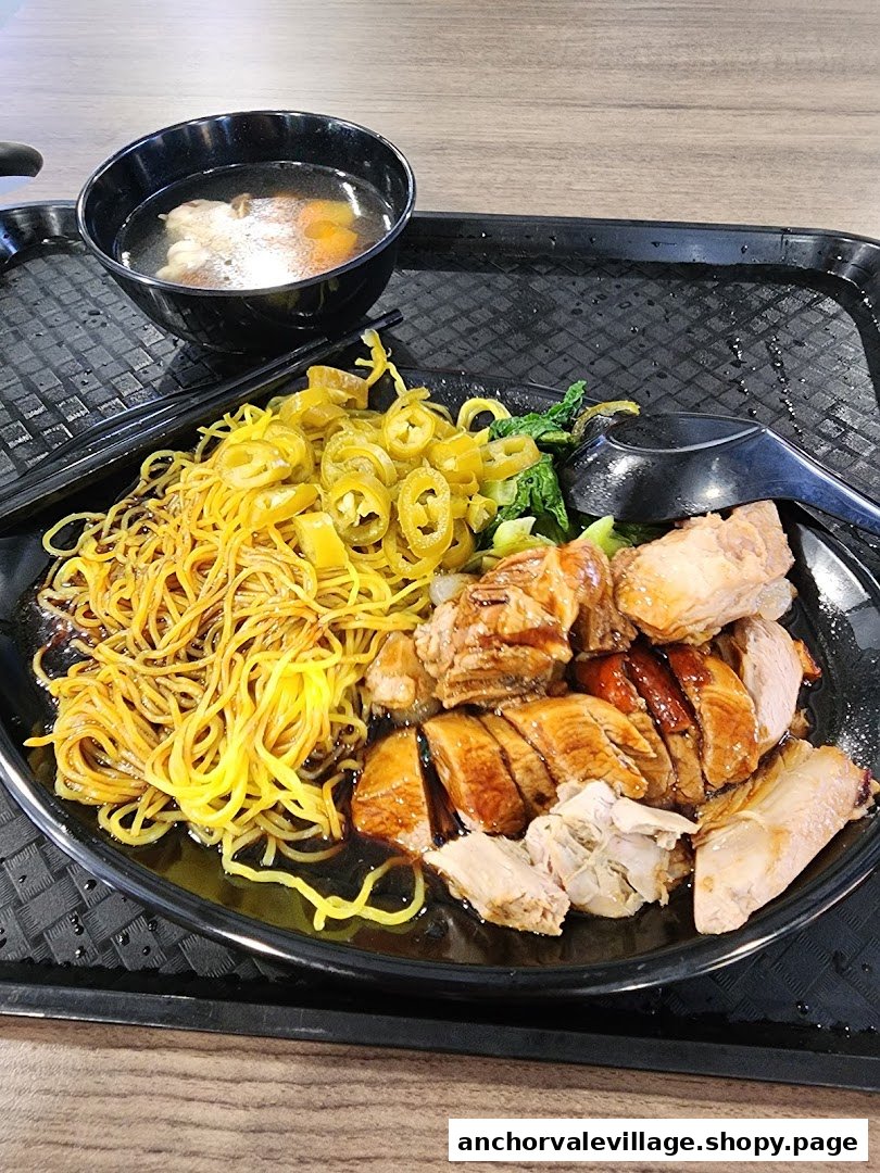 A close-up of a delicious plate of roasted duck and char siew noodles with pickled chillies and a side of soup.