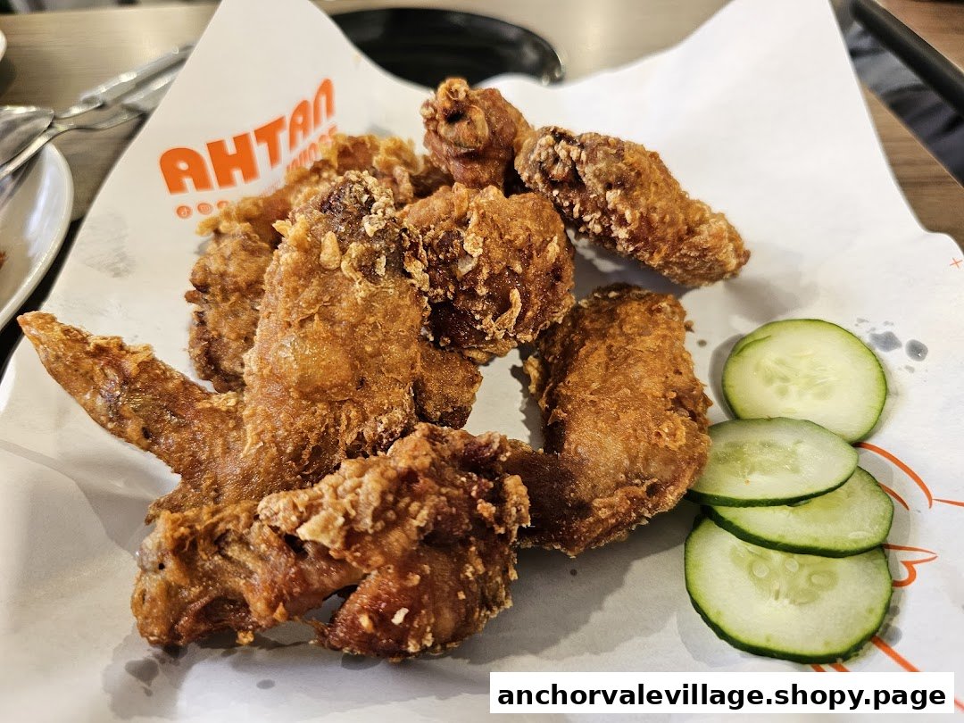 A plate of crispy fried chicken wings with cucumber slices, served on white paper.