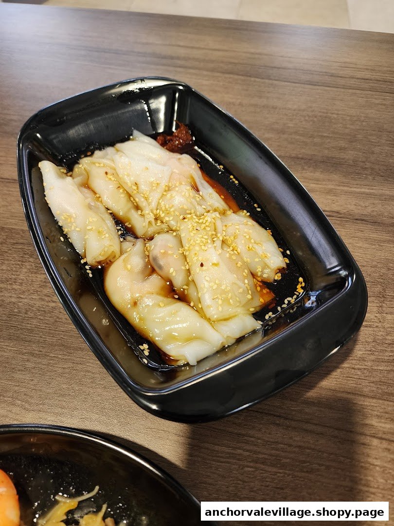A close-up of delicious Chee Cheong Fun with soy sauce and sesame seeds in a black dish.