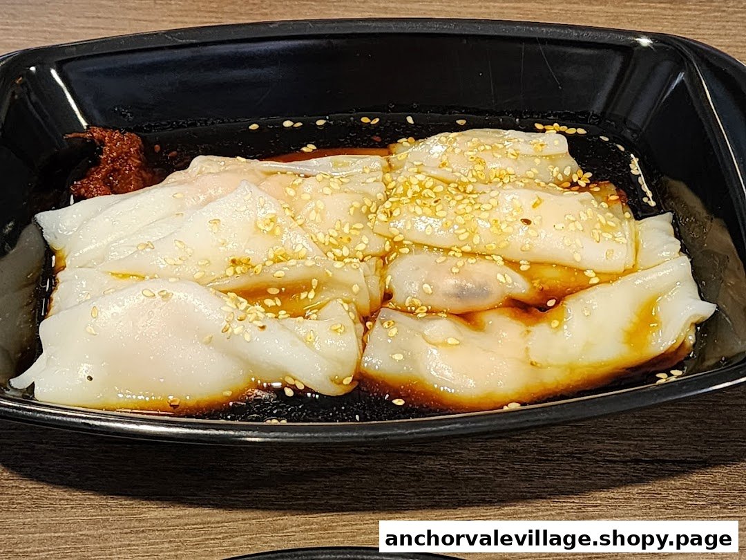 A close-up of delicious Chee Cheong Fun with savory sauce, sesame seeds, and chili paste in a black bowl.