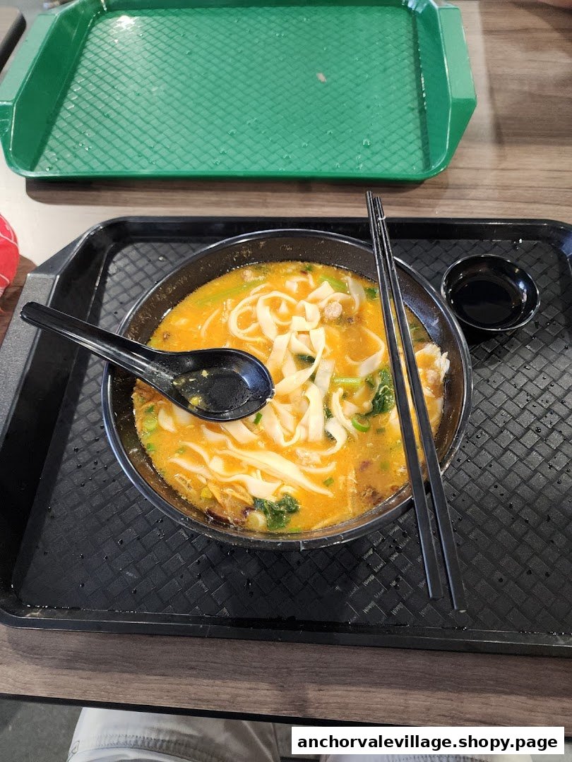 A close-up of a bowl of noodles with a rich broth, spoon, and chopsticks on a black tray.