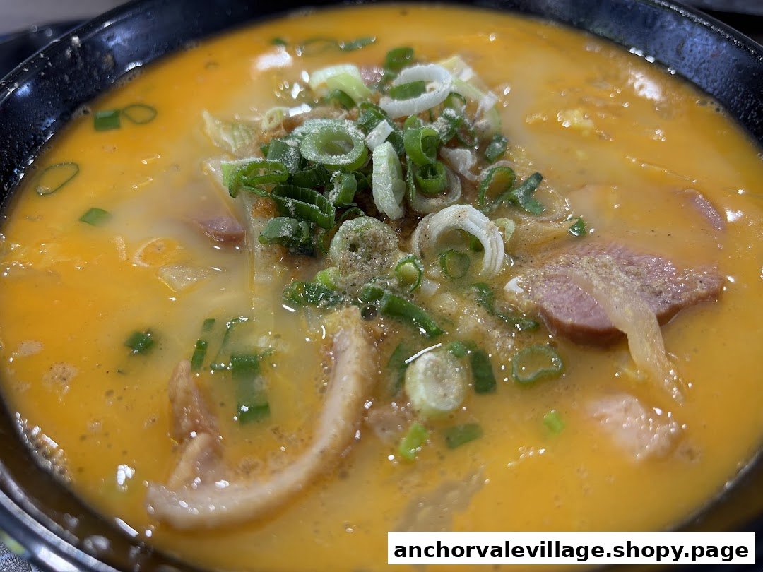 A close-up of a vibrant bowl of noodles with a rich orange broth, topped with green onions and various ingredients.