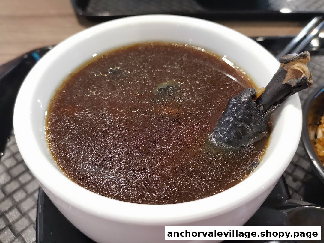 A close-up of a bowl of dark, bubbling soup with a black chicken leg.