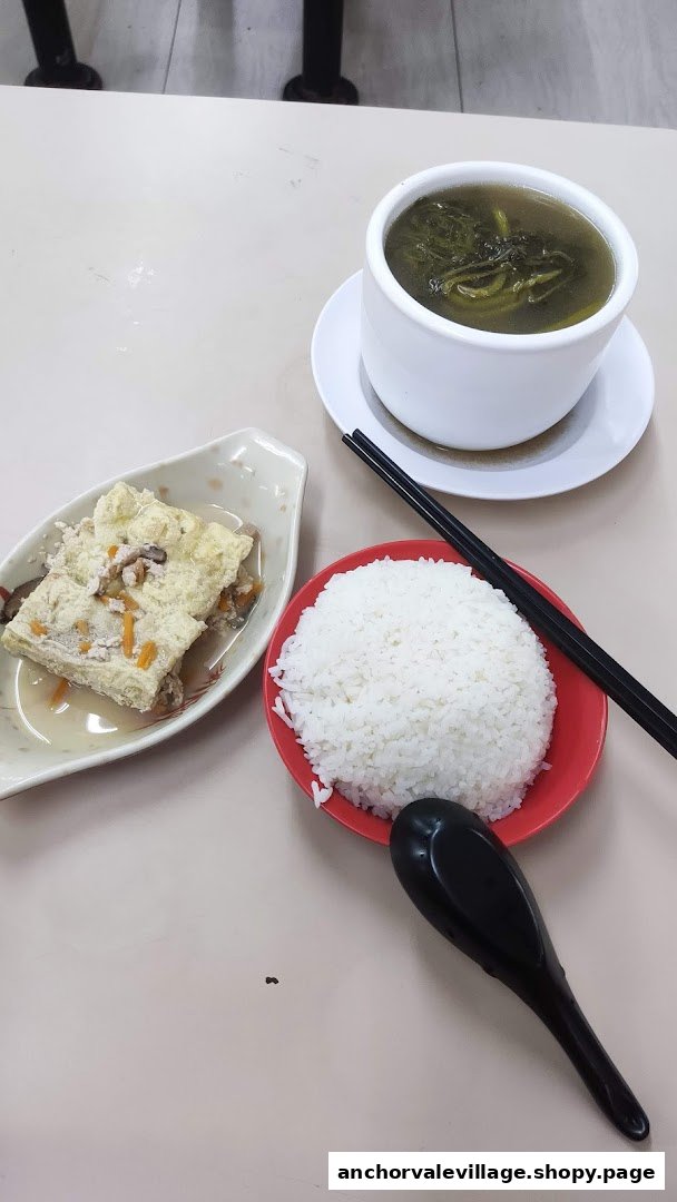 A comforting meal featuring a bowl of soup, a plate of rice, and a side dish of stuffed tofu.