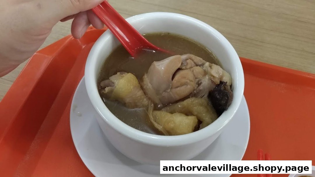 A close-up of a nourishing bowl of chicken soup with mushrooms, served on an orange tray.