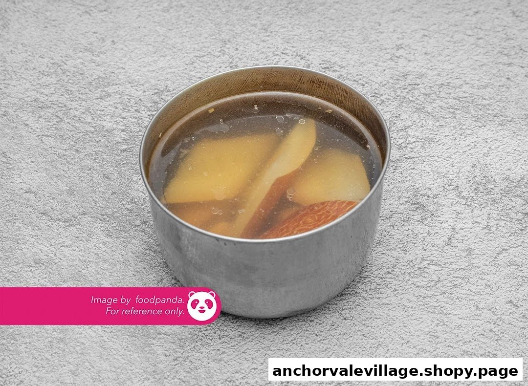 A close-up of a metal bowl filled with clear soup and fruit slices.