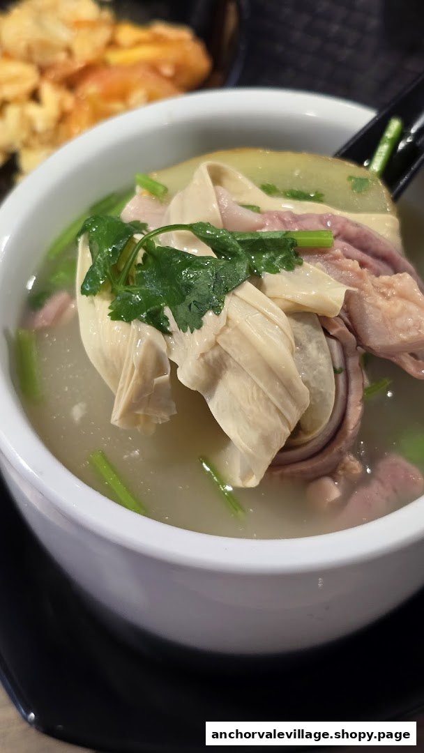 A close-up of a hearty Chinese soup with tofu skin, meat, and green vegetables in a white bowl.