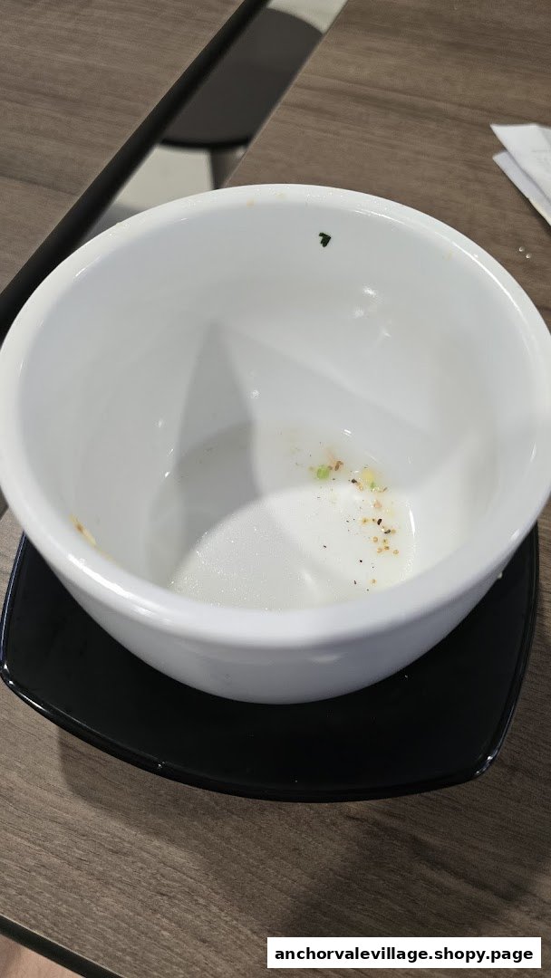 An empty white soup bowl with a few remnants on a black saucer, placed on a wooden table.