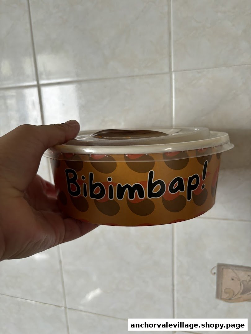 A hand holds a takeout container featuring the "Bibimbap!" logo against a tiled background.