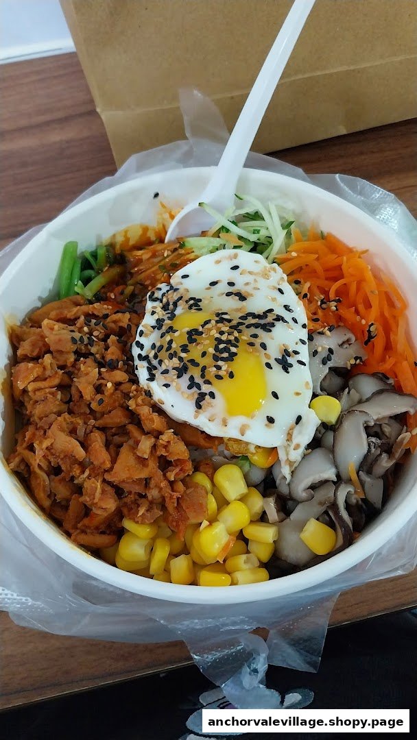 A vibrant bibimbap bowl featuring various fresh ingredients, a fried egg, and a plastic spoon, ready to eat.