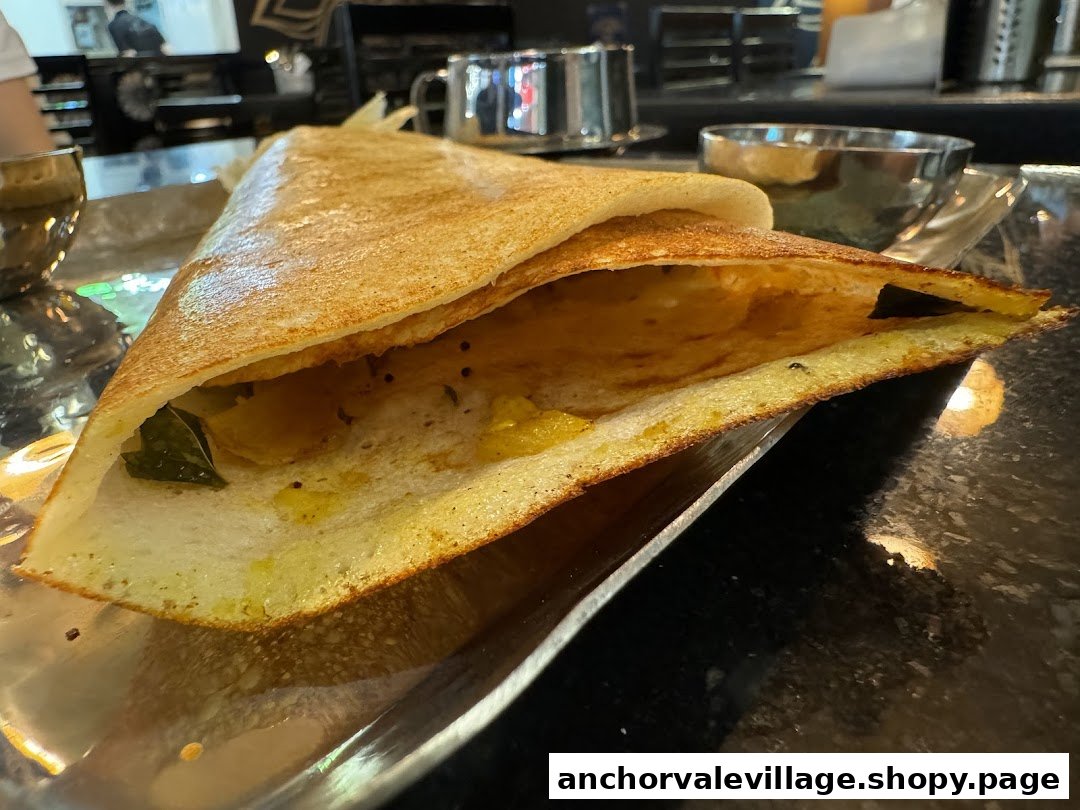 A close-up of a golden-brown dosa filled with potato masala, served on a metal plate.