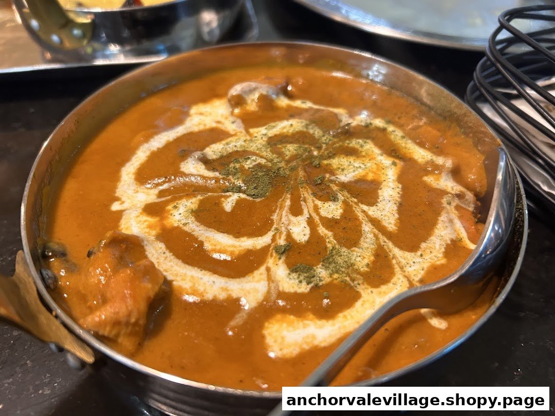 A close-up of a rich, creamy orange curry dish, garnished with cream swirls and green herbs.