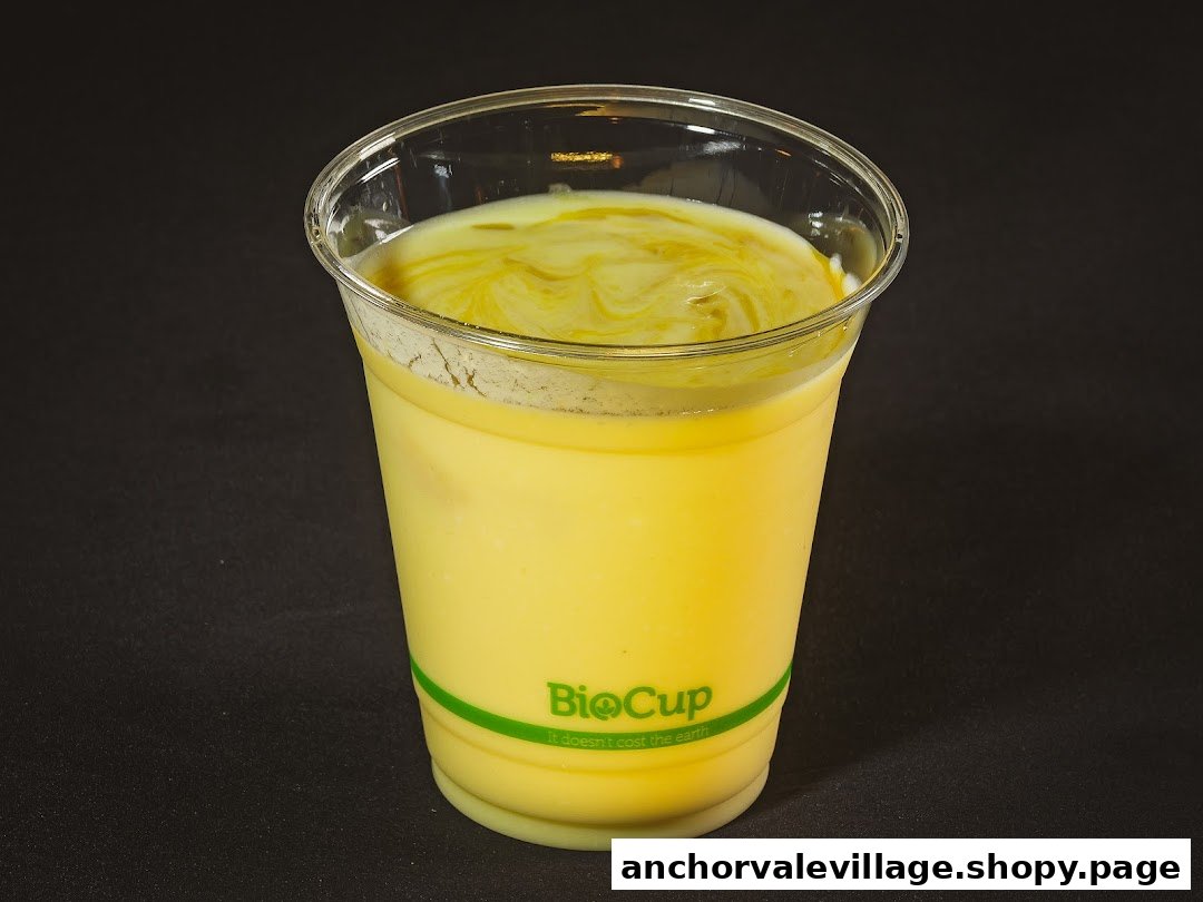 A vibrant yellow beverage, possibly a mango lassi or milkshake, in a clear BioCup with a swirl on top.