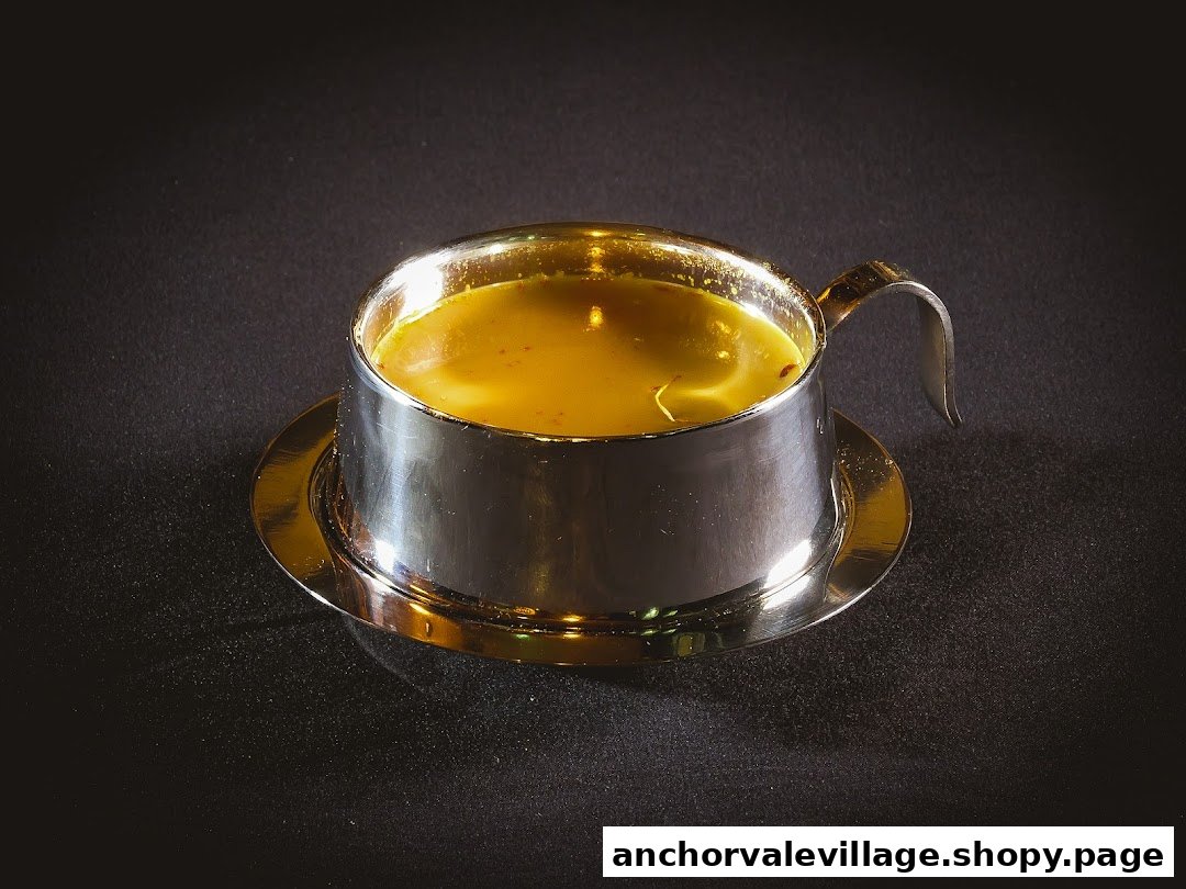 A golden, aromatic broth or soup served in a polished metallic cup with a matching saucer.