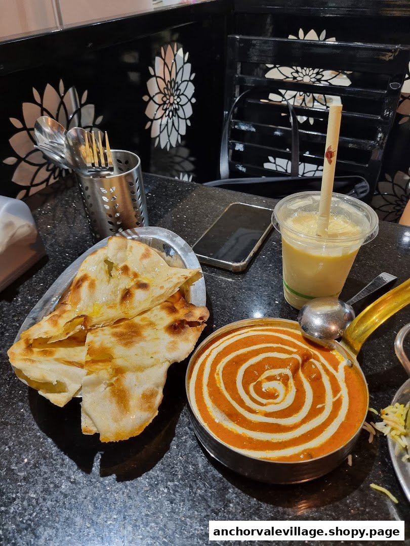 A delicious meal featuring naan bread, creamy curry, and a refreshing drink on a black speckled table.