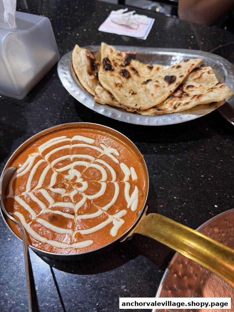 A vibrant Indian curry dish with cream art and a side of freshly baked naan bread.
