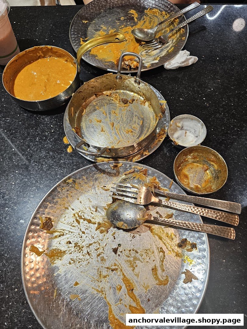Empty plates and bowls on a table after a delicious meal, showing remnants of biryani and curry.