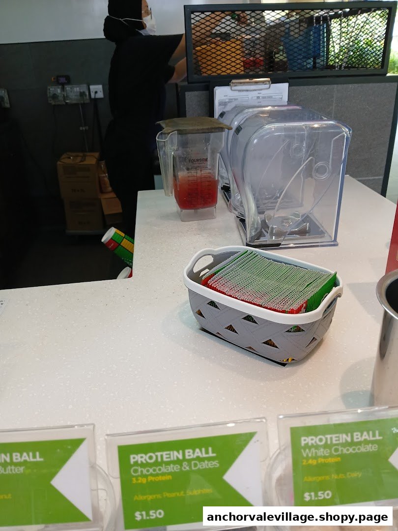 A staff member prepares a drink at the counter, with blenders and protein balls on display.