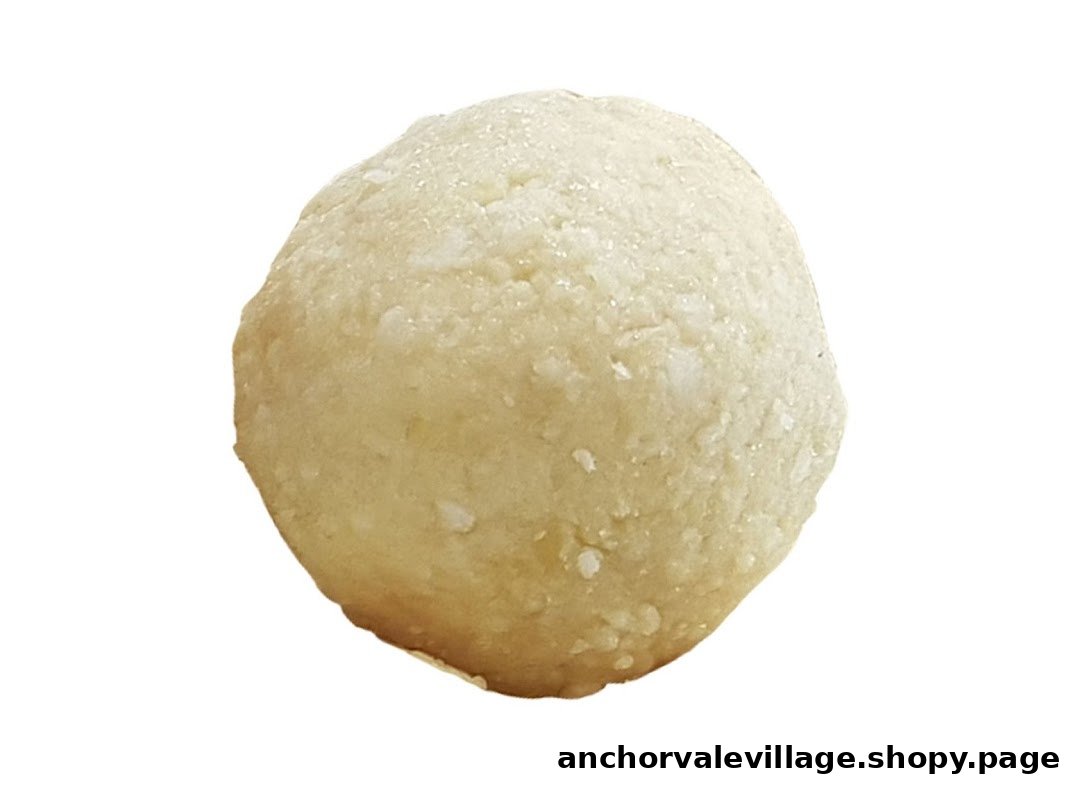A close-up of a spherical, light-colored sweet or dessert item, possibly a coconut laddu or cookie dough.