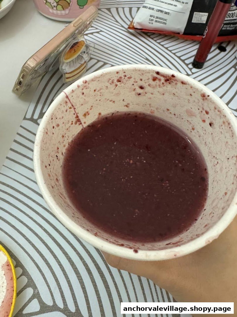 A close-up of a dark berry-colored smoothie or juice in a white cup.