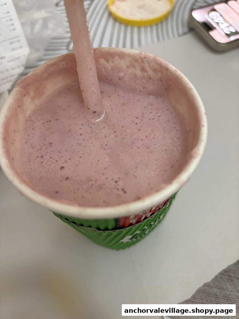 A close-up of a pink, frothy smoothie with a straw in a branded Boost Juice cup.