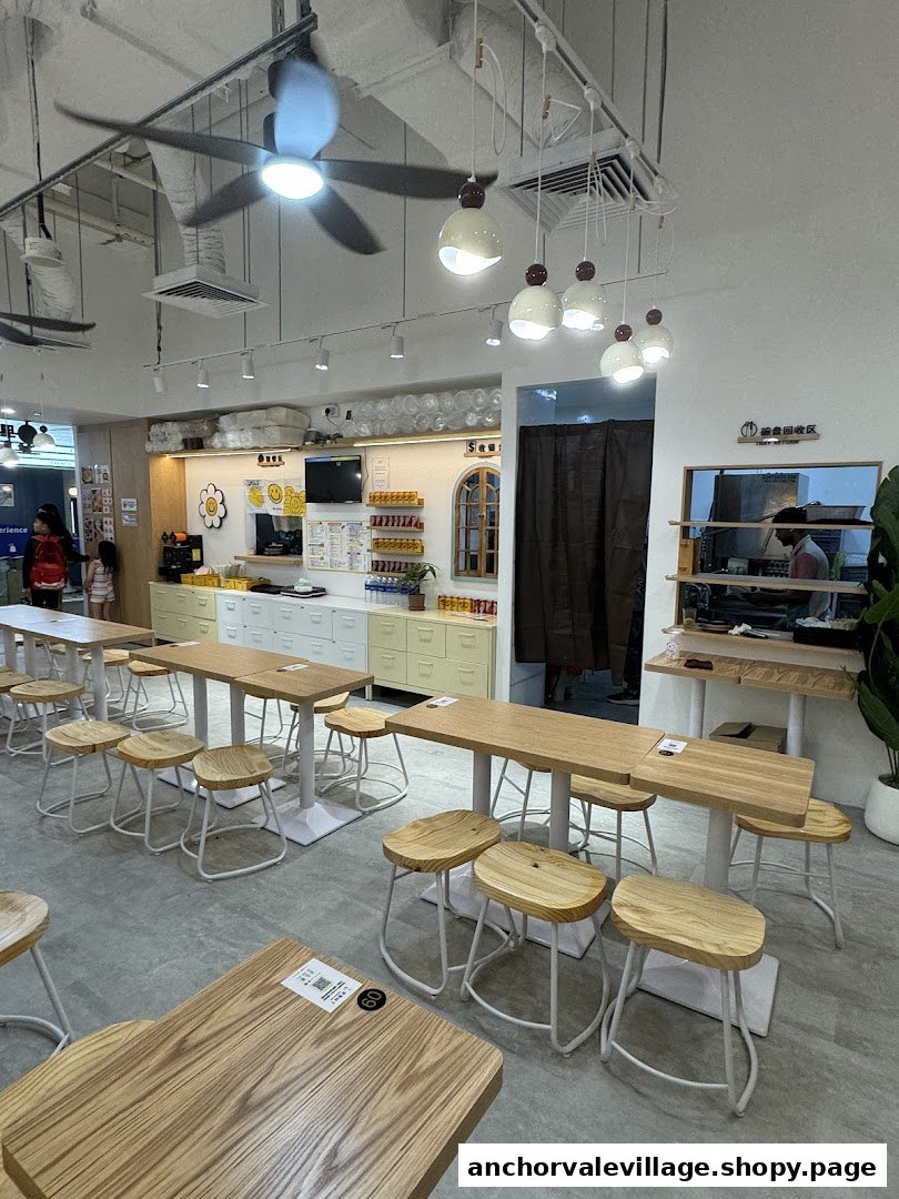 Interior view of a bright, modern cafe with wooden tables, stools, and a service counter.