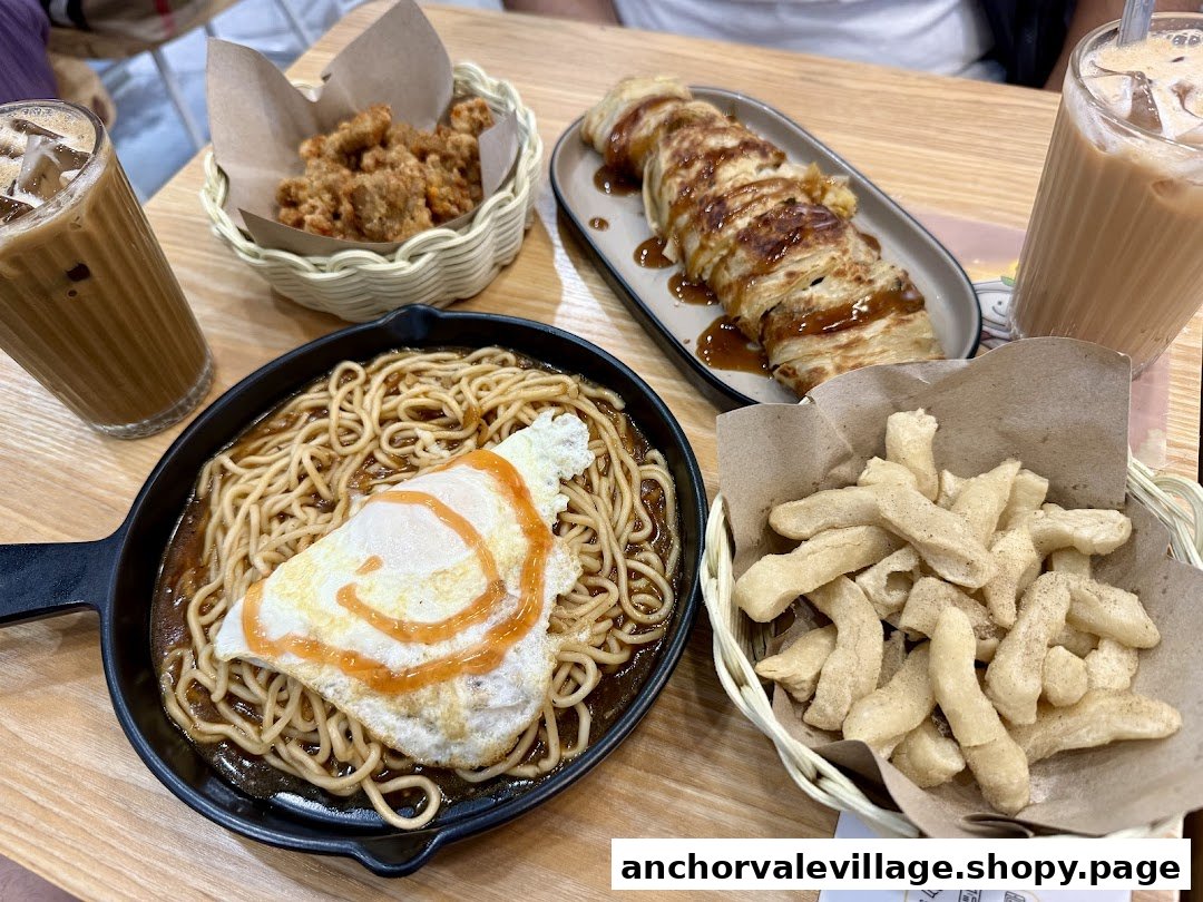 A table laden with delicious breakfast items including noodles, fried chicken, crispy snacks, and iced beverages.