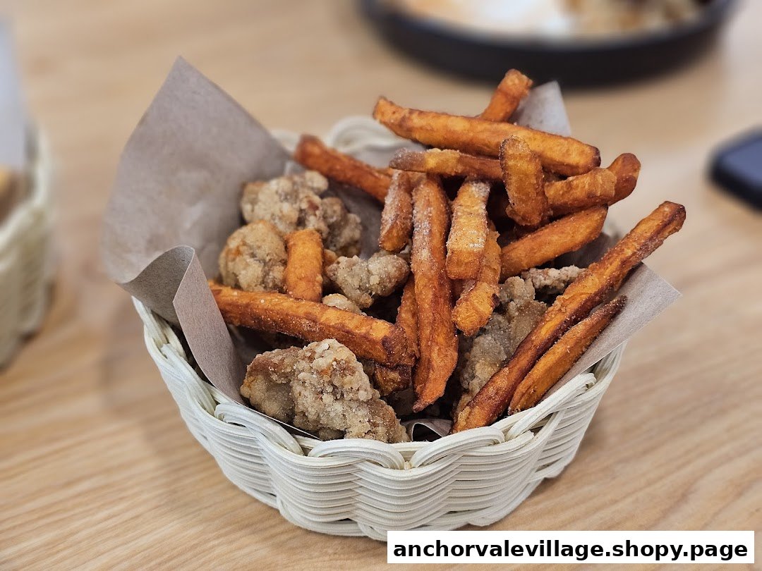 A basket of crispy sweet potato fries and fried chicken pieces on a wooden table.